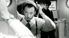 a man in a suit and tie is looking at himself in a mirror while a police officer stands in the background