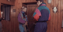 a man in a colorful jacket is standing in a room with wood paneling and skulls on the wall .