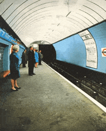 a group of people waiting for a train at a station with a sign on the wall that says ' underground ' on it