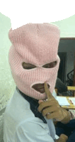 a person wearing a pink ski mask is holding their finger to their lips .