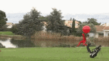 a man in a red suit is carrying a golf bag and a red balloon on a golf course .