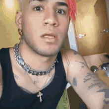 a man with pink hair is wearing a black tank top and a silver cross necklace