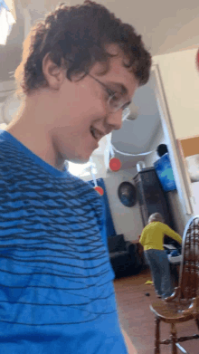 a boy wearing glasses and a blue shirt is standing in a living room