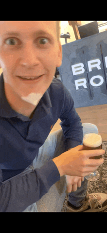 a man is holding a glass of beer in front of a sign that says brio