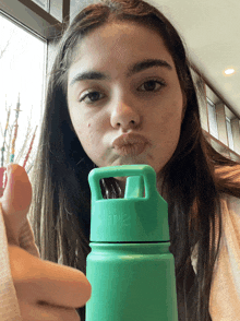 a girl is holding a green water bottle with a straw and making a funny face