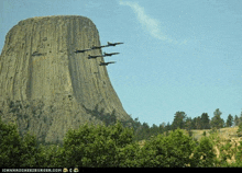 a group of fighter jets flying over a large rock formation with trees in the foreground