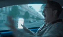 a man is screaming while holding a cell phone in his hand while driving a car .