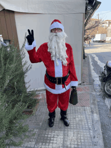 a man dressed as santa claus giving a peace sign while holding a bell