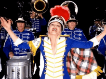 a woman in a marching band uniform stands in front of a silver yamaha drum