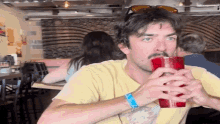 a man with a mustache is drinking from a red cup in a restaurant