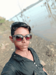 a young man wearing sunglasses takes a selfie in front of a body of water on the date of 2020/9/1