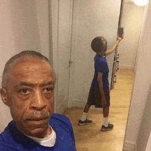 a man is taking a selfie in front of a mirror while a boy is taking a selfie in the background .