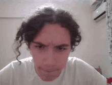 a man with curly hair is making a funny face while wearing a white shirt .