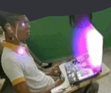 a man wearing headphones is sitting in front of a laptop with a purple light coming out of it .