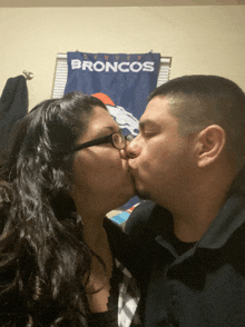 a man and a woman kiss in front of a denver broncos flag