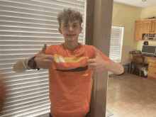 a young man in an orange shirt is giving a thumbs up sign