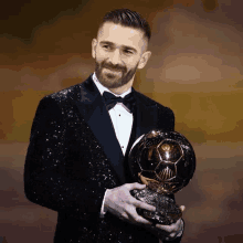 a man in a tuxedo holds a trophy in his hand