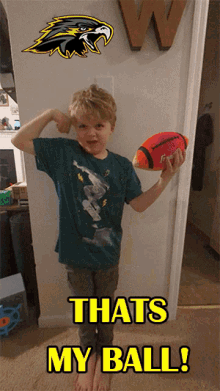 a young boy is holding a football and flexing his muscles in front of a wall that says that 's my ball