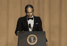 a man in a tuxedo is standing at a podium with the seal of the president of the united states on it