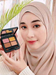 a woman in a hijab is holding a palette of eye shadows