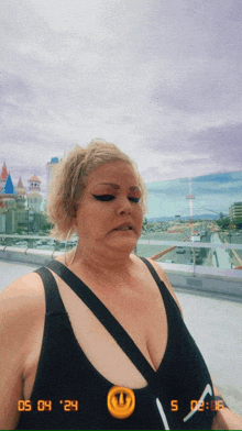 a woman in a black tank top is standing in front of a city with a time stamp of 05 04 24