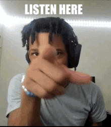 a man wearing headphones is pointing at the camera with the words listen here below him