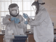 two scientists wearing protective suits and masks are putting on gloves in a laboratory .