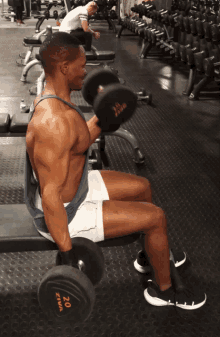 a man sits on a bench holding a dumbbell that says 20