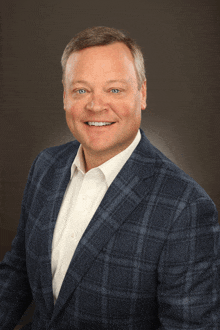 a man wearing a blue plaid suit and white shirt smiles for the camera