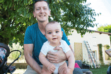 a man in a blue shirt holds a baby in his lap