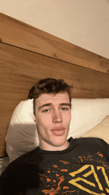 a young man is laying on a bed wearing a black shirt with a yellow and black triangle on it