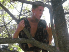 a shirtless man is sitting on a tree branch looking at something