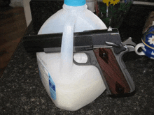 a gun rests on top of a gallon of milk on a counter