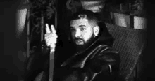 a black and white photo of a man with a beard sitting in a chair .