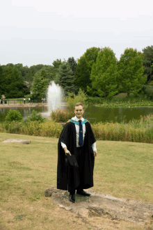 a man in a graduation gown stands in front of a lake