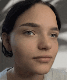 a close up of a woman 's face with blue eyes and a white shirt on .