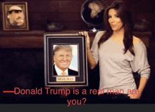 a woman holds a framed picture of donald trump with the caption " donald trump is a real man are you "