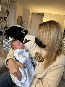 a woman is holding a baby wearing a polo bear sweater