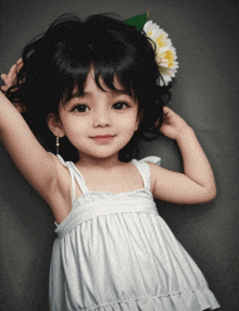 a little girl wearing a white dress and a flower in her hair