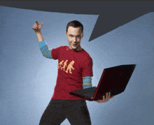 a man wearing a red shirt that says big bang holds a laptop