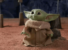 a baby yoda toy is standing on a dirt surface