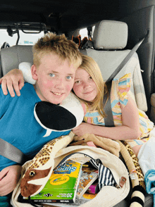 a boy and a girl are sitting in the back seat of a car with a bag of crayola super wipes