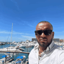 a man wearing sunglasses stands in front of boats in a harbor