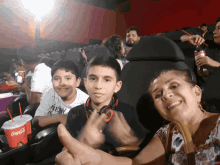 a woman giving a thumbs up while sitting in a movie theater with two children and a coca cola cup