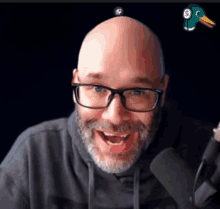 a bald man with glasses and a beard stands in front of a microphone