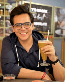 a man wearing glasses holds a drink in front of a sign that says t's more chocolate