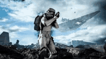 a stormtrooper is kneeling down on a rocky hill holding a gun in front of a star destroyer .