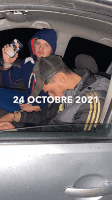 two men are sitting in a car with the date 24 october 2021