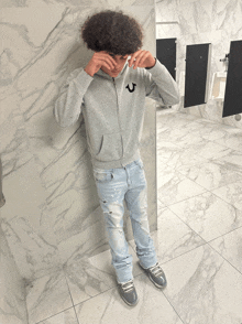 a man wearing a grey true religion hoodie covering his face