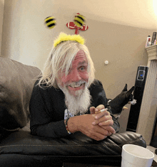 a man wearing a bee headband sits on a couch smoking a cigarette